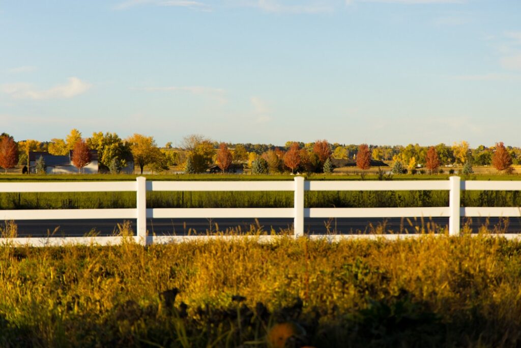 Two people discuss a boundary line on a rural property with a fence, trees, and open pastureland in the background.