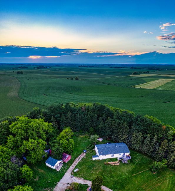 A couple walks along a grassy rural property, reviewing papers and inspecting open farmland with wooded borders in the distance.